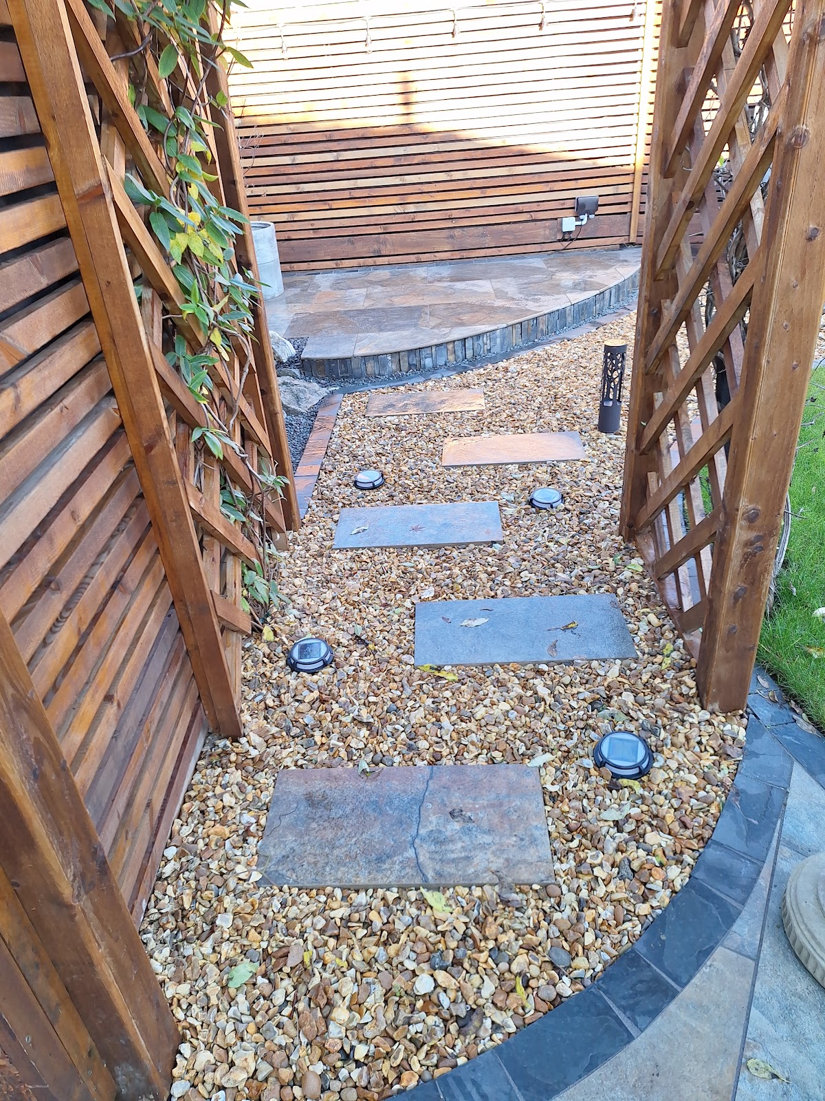 A landscaped garden path with stepping stones, gravel and timber trellis screening